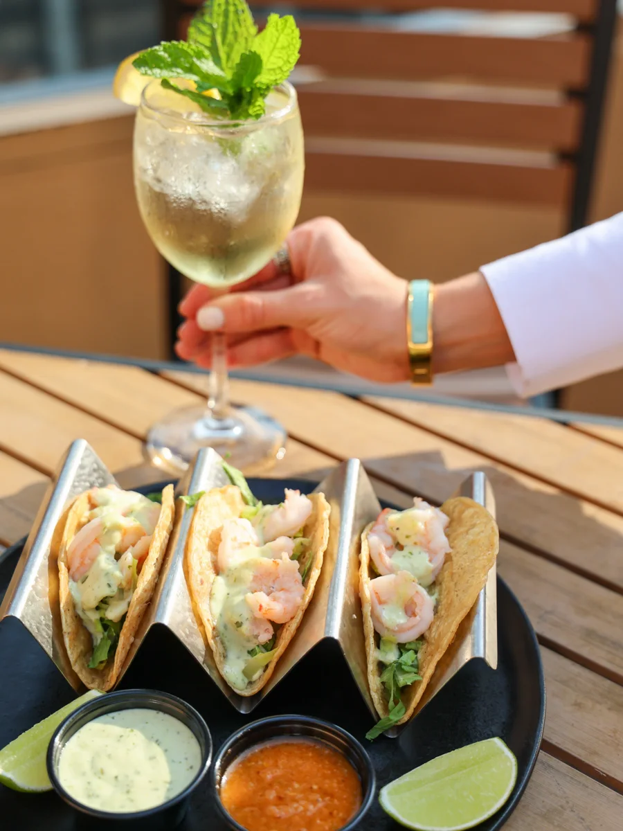 A guest enjoying a cocktail alongside shrimp tacos at SkyDeck at Twenty Nine